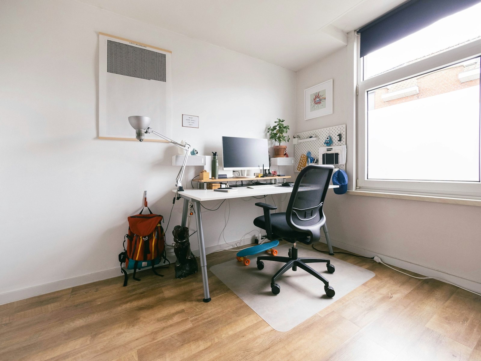 Home office desk set up beneath a window with a monitor and chair